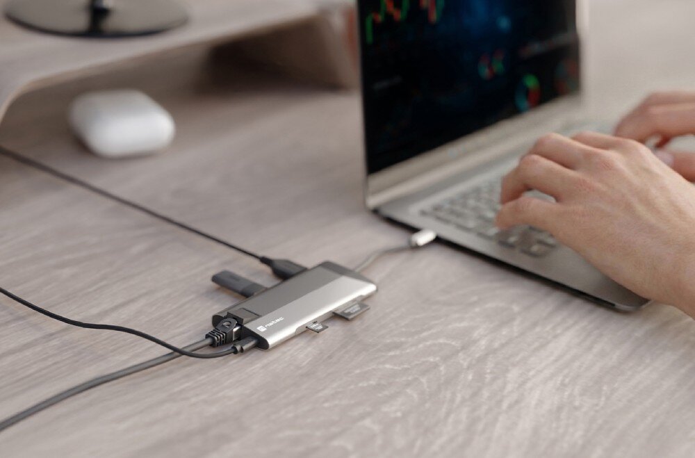 Hub NATEC Fowler Plus 8w1 Osoba korzysta z laptopa podłączonego do stacji dokującej na drewnianym stole.
