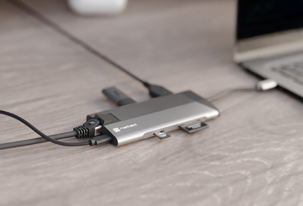 Hub NATEC Fowler Plus 8w1 Urządzenie z różnymi portami podłączonymi do laptopa na drewnianym biurku.