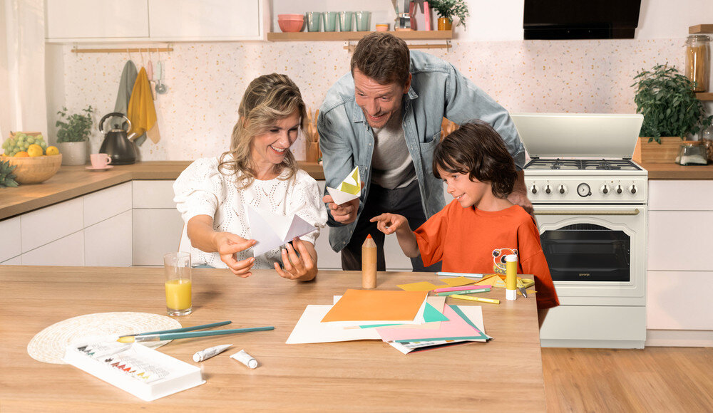 KUCHNIA GORENJE GKS5B70CLI lifestyle kuchnia rodzina dziecko akcesoria plastyczne na stole kuchenka w tle kolor czarno srebrny okap półki czajnik akcesoria kuchenne na blacie