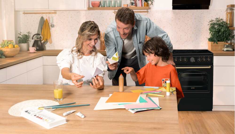 KUCHNIA GORENJE GECS5B70CLB lifestyle kuchnia rodzina dziecko akcesoria plastyczne na stole kuchenka w tle kolor czarno srebrny okap półki czajnik akcesoria kuchenne na blacie