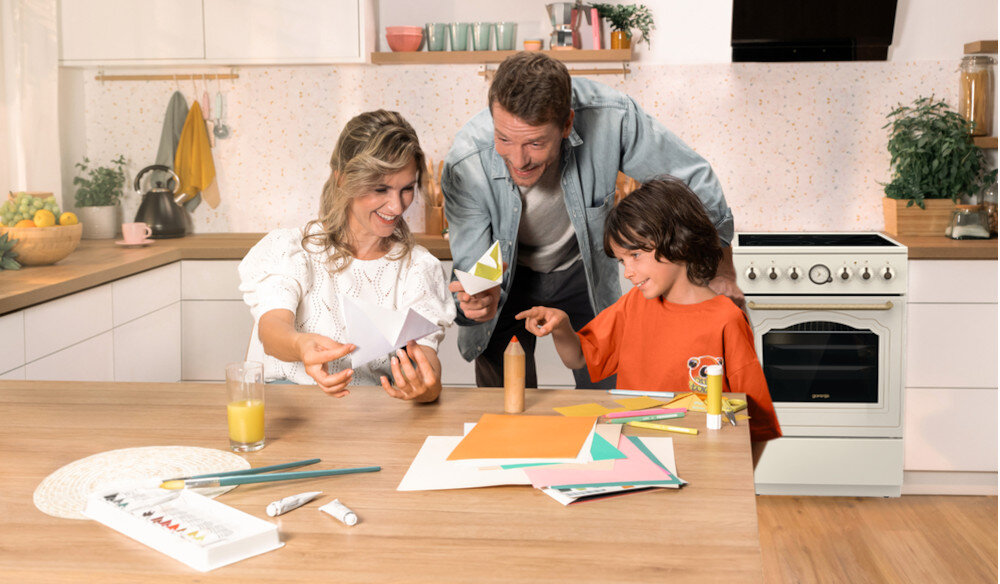 KUCHNIA GORENJE GECS5B70CLI lifestyle kuchnia rodzina dziecko akcesoria plastyczne na stole kuchenka w tle kolor czarno srebrny okap półki czajnik akcesoria kuchenne na blacie