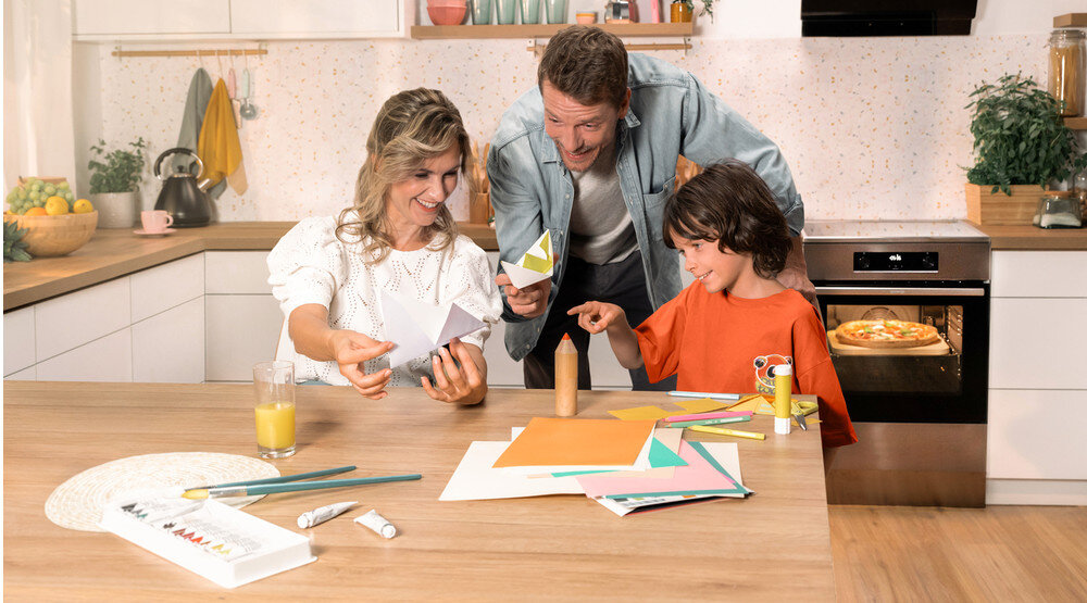 KUCHNIA GORENJE GEIT5C61XPG lifestyle kuchnia rodzina dziecko akcesoria plastyczne na stole kuchenka w tle kolor czarno srebrny okap półki czajnik akcesoria kuchenne na blacie