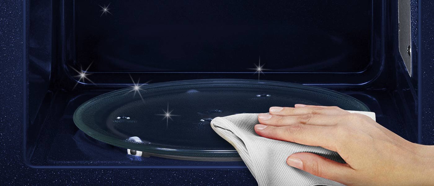 Zbliżenie na dłoń przecierającą za pomocą ściereczki wnętrze mikrofali Zbliżenie na dłoń przecierającą za pomocą ściereczki wnętrze mikrofali