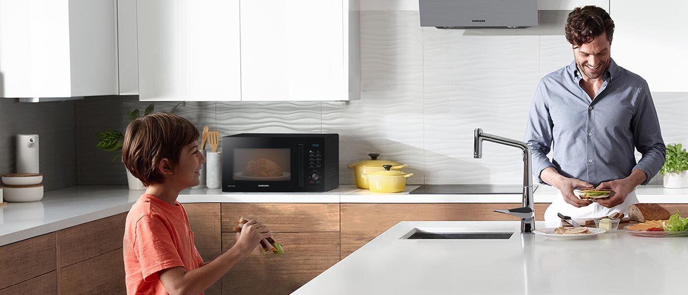 Mężczyzna i chłopiec jedzą kanapki, a w kuchence mikrofalowej przygotowuje się kolejne danie Mężczyzna i chłopiec jedzą kanapki, a w kuchence mikrofalowej przygotowuje się kolejne danie