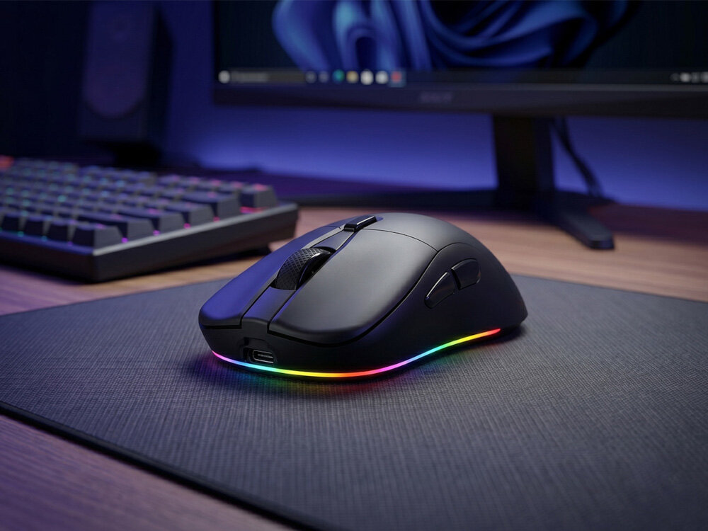 Czarna mysz gamingowa z podświetleniem RGB na podkładce, obok klawiatury i monitora.