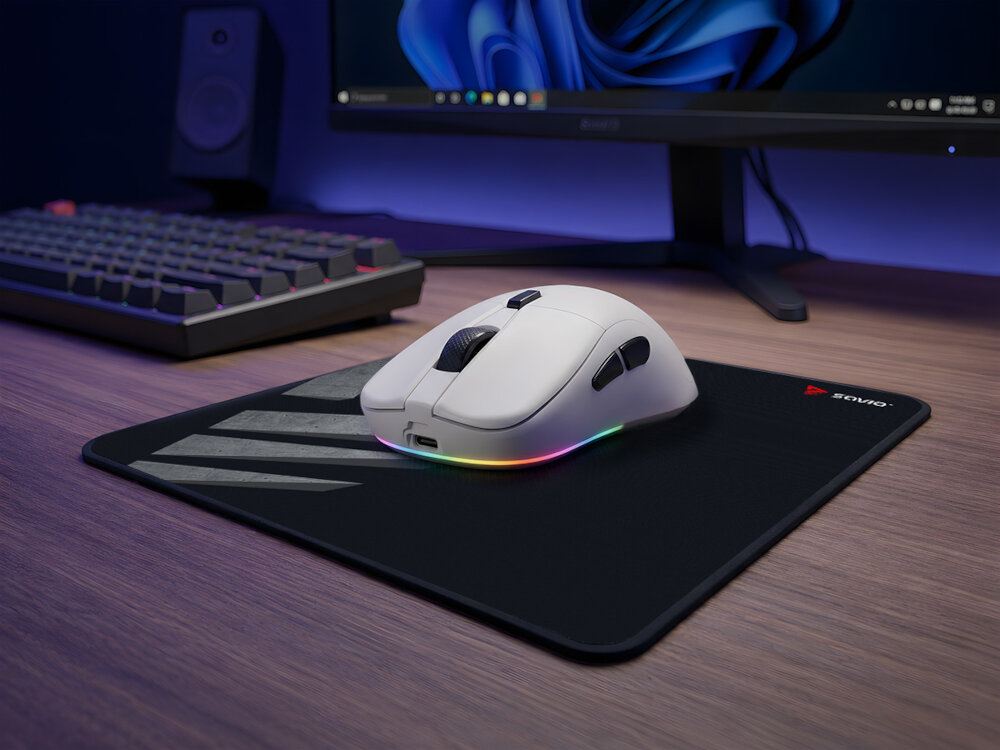 Biała mysz gamingowa z podświetleniem RGB na podkładce przy monitorze.
