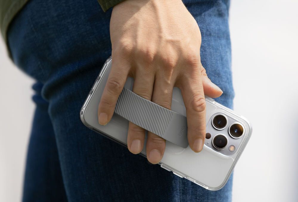 Osoba trzyma telefon z przezroczystym etui, które ma szary uchwyt na palce. Telefon ma trzy widoczne obiektywy aparatu.