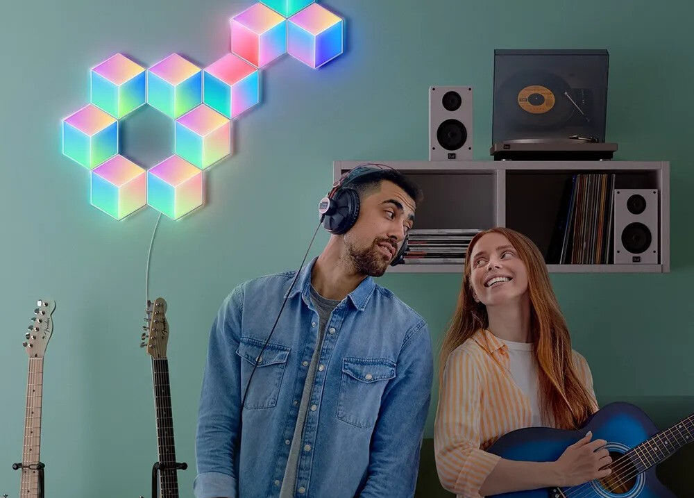 Panel świetlny GOVEE H6066 Glide Hexa Pro Wi-Fi + Bluetooth panele na ścianie kobieta grająca na gitarze obok mężczyzna w słuchawkach Personalizacja animacji i kolorów na sześciokątnych panelach świetlnych