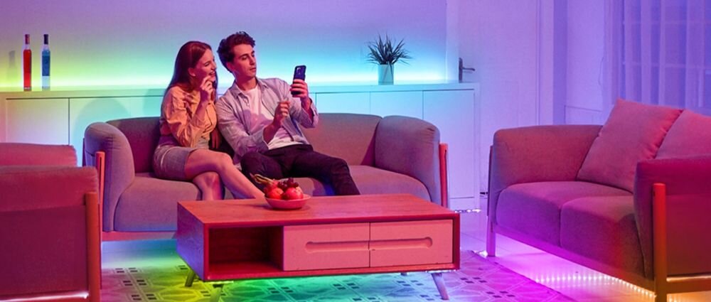 Taśma LED GOVEE H615A 5m Wi-Fi, taśma, RGB, dekoracja, nastrój, Para na sofie z kolorowym oświetleniem LED pod meblami.