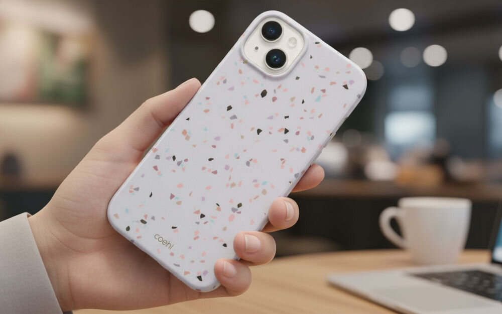Osoba trzyma telefon w etui z wzorem terrazzo w pastelowych kolorach. Na etui widoczny jest napis \'coehl\'.