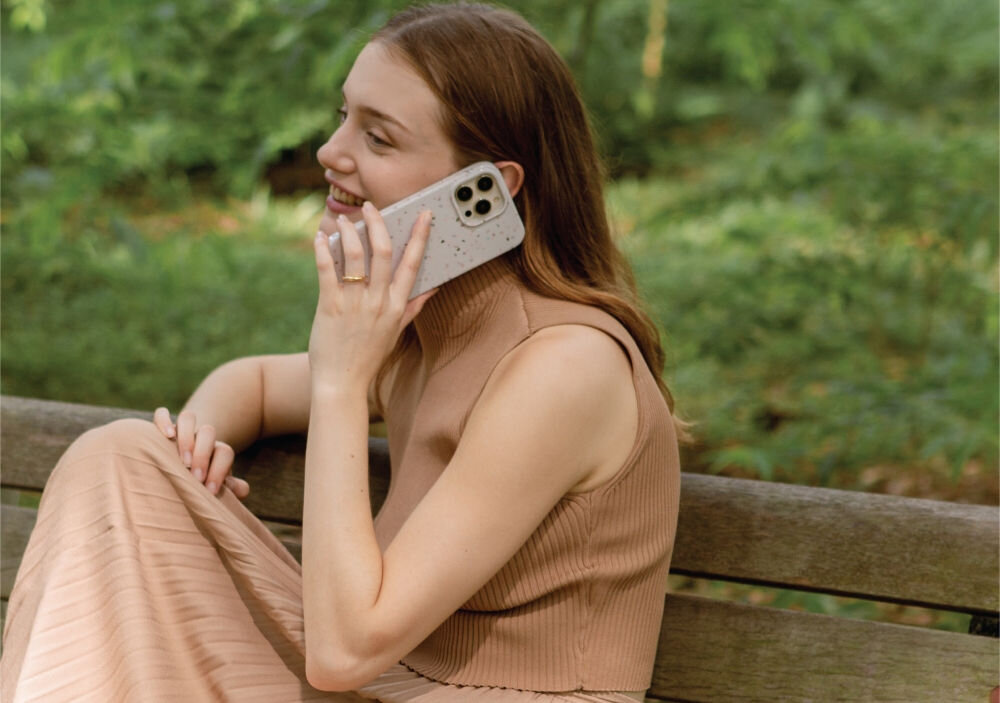 Osoba siedzi na ławce w parku, trzymając telefon z etui o wzorze terrazzo. W tle widoczna jest zielona roślinność.