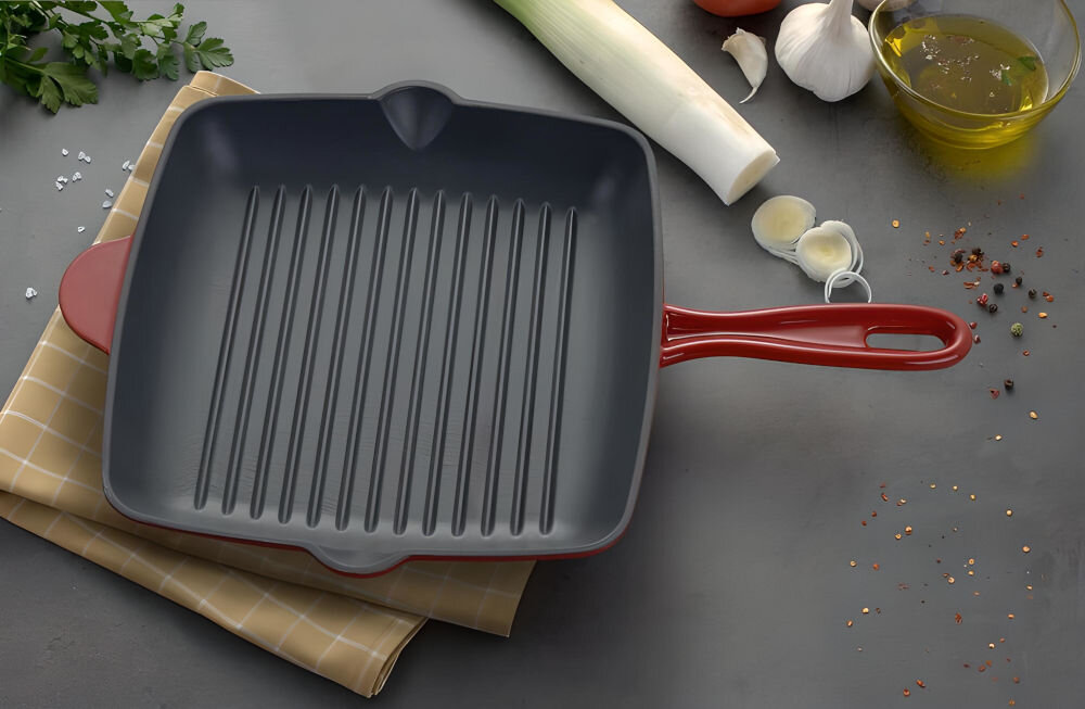 Patelnia MG HOME Infinito 26 cm patelnia położona na ścierce ciemny środek wyżłobienia czerwona na zewnątrz leży na ciemnym blacie średnica 26 cm wysoka jakość wykonania solidne żeliwo pokryta wewnątrz emalią trwałość smażenie zapiekanie żeliwo wytrzymałość odporność na wysokie temperatury bez utraty właściwości 