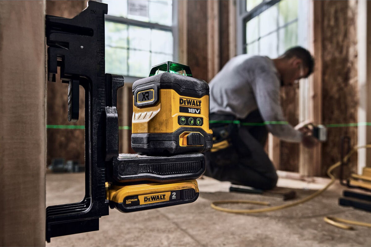 Laser krzyżowy DEWALT DCLE34031D1-QW, mierzenie, laser, odległość, budowa, laser zamontowany do ściany na uchwycie, w tle mężczyzna na budowie