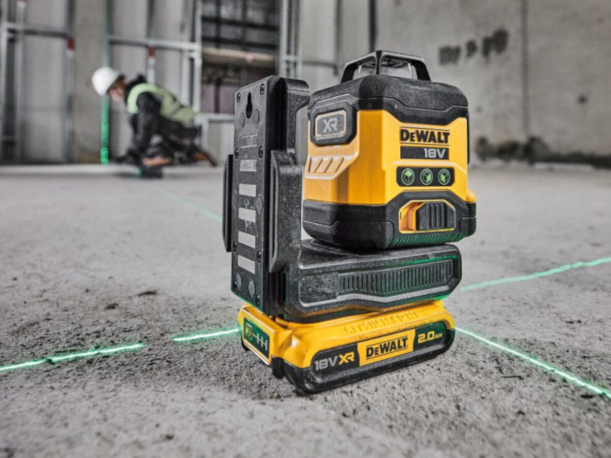 Laser krzyżowy DEWALT DCLE34031D1-QW, linie, pion, poziom, obrót, 360, laser stoi na podłodze betonowej, w tle pracownik budowy