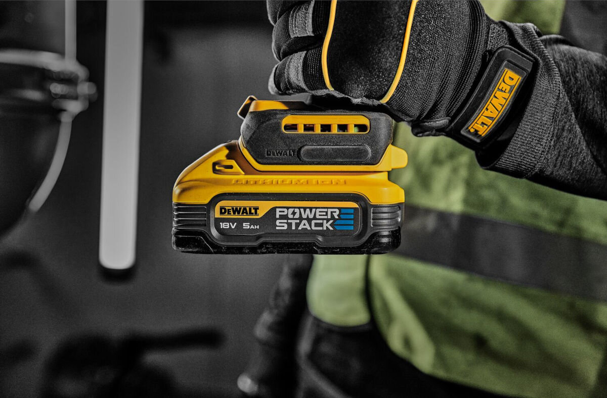 Akumulator DEWALT DCBP518 5Ah 18V, ładowanie, praca, zasilanie, energia, w tle osoba w kamizelce roboczej trzyma narzędzie z podłączonym akumulatorem
