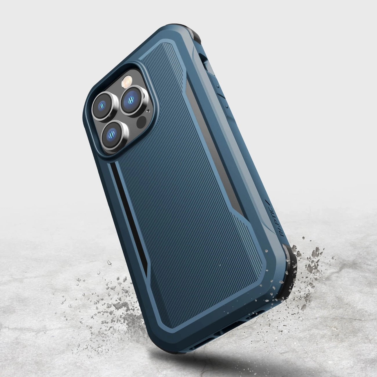 Niebieskie etui ochronne na telefon z widocznymi trzema obiektywami aparatu i lampą błyskową. Etui ma teksturowaną powierzchnię i jest przedstawione na tle imitującym beton z unoszącymi się drobinkami kurzu.