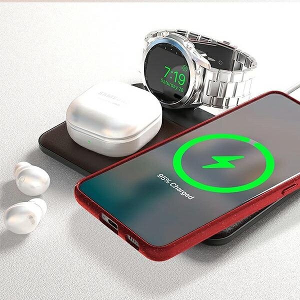 Na obrazie widać smartfon w czerwonym etui z wyświetlaczem pokazującym ikonę ładowania i napis \'95% Charged\'. Obok znajdują się bezprzewodowe słuchawki, etui ładujące z logo \'Samsung\' oraz zegarek z wyświetlaczem pokazującym godzinę 7:19.