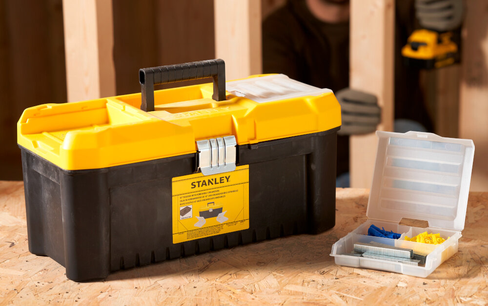 Skrzynka narzędziowa STANLEY Essential 16‘’ STST75785-1 skrzynka wypełniona narzędziami obok tacka drewniany blat w tle drewniana ściana porządek transport mobilność przenoszenie narzędzi