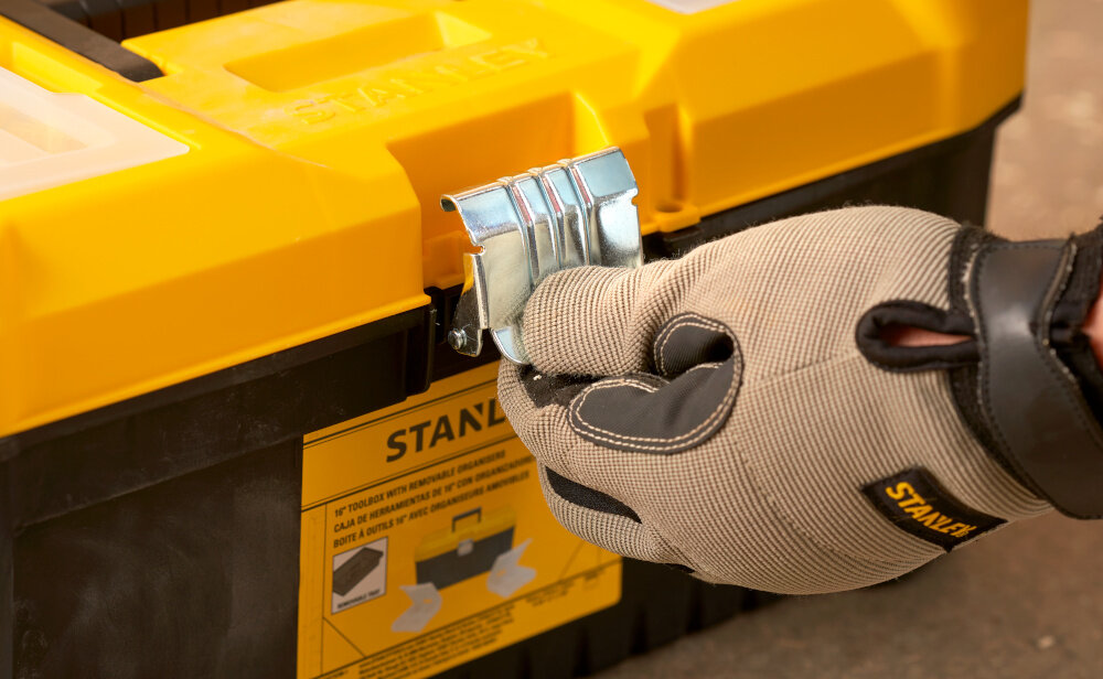 Skrzynka narzędziowa STANLEY Essential 16‘’ STST75785-1 zbliżenie na zamek osoba trzyma zamek w palcach solidny metalowy zamek bezpieczne przechowywanie narzędzi i akcesoriów ochrona zawartość przed przypadkowym otwarciem trwałość