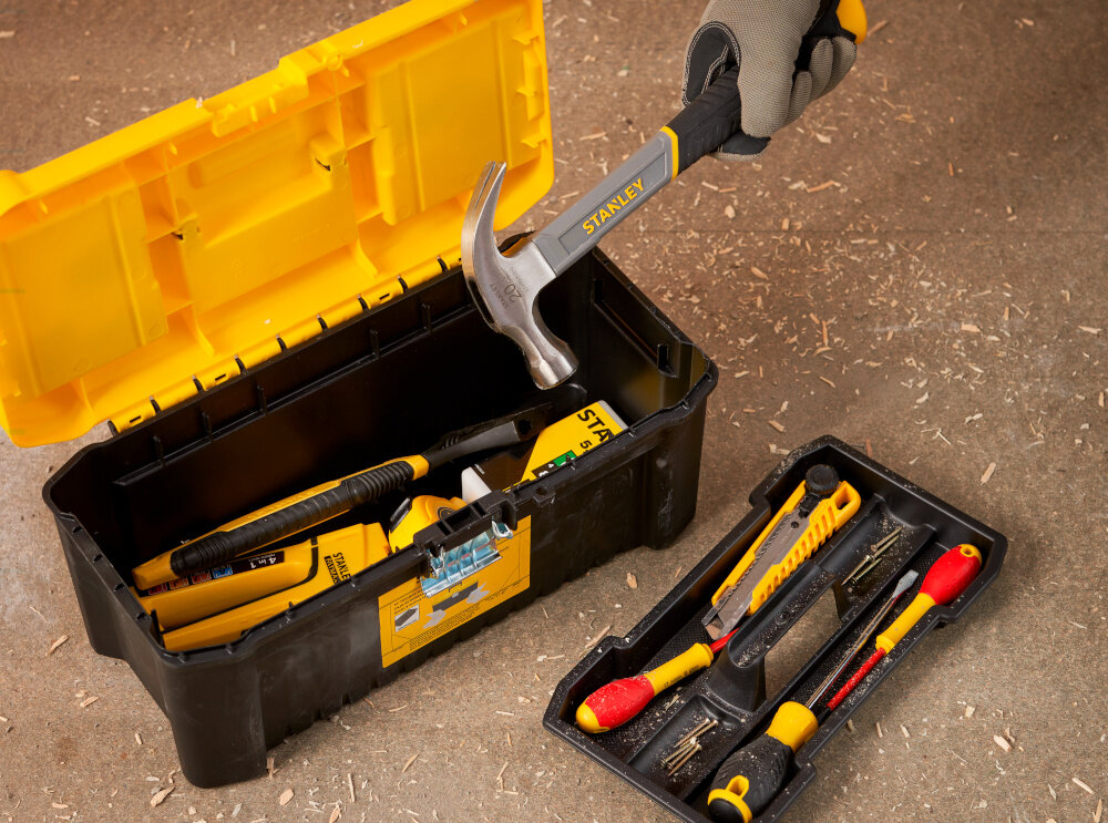 Skrzynka narzędziowa STANLEY Essential 16‘’ STST75785-1 skrzynka na drewnianym blacie obok tacka narzędzia w tle drewniana ściana wygodne przechowywanie narzędzi i akcesoriów porządek w miejscu pracy duża pojemność wnętrza 8 litrów efektywność komfort