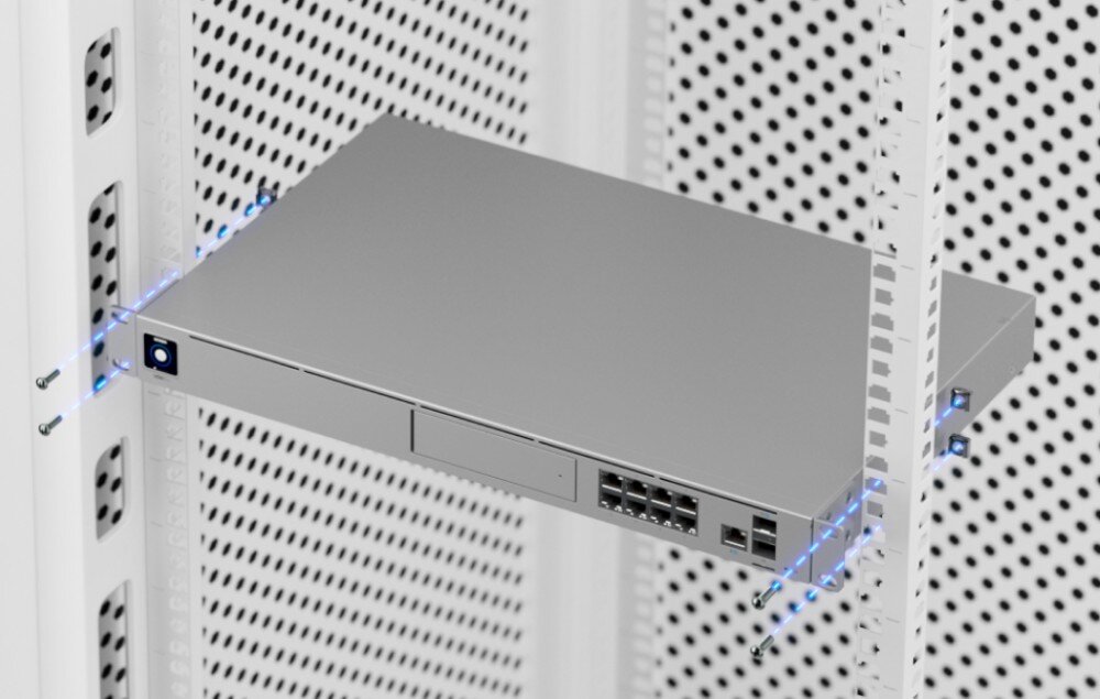 Router UBIQUITI UDM-SE-EU Ilustracja techniczna pokazująca proces montażu urządzenia w białej szafie serwerowej z zaznaczonymi niebieskimi liniami miejscami na śruby