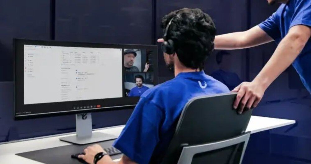 Router UBIQUITI UDM-SE-EU Dwie osoby w biurze analizujące dane na panoramicznym monitorze wyświetlającym interfejs systemu zarządzania oraz podgląd z kamer wideo