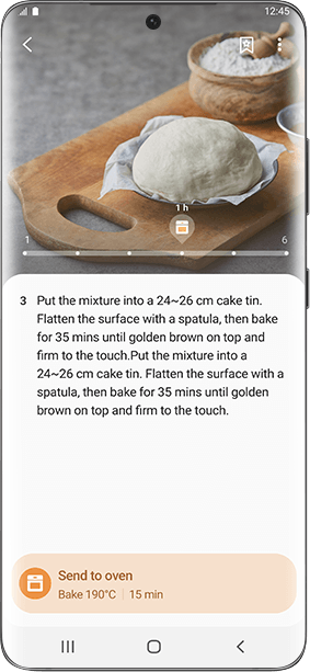 Na ekranie smartfona widoczny jest przepis kulinarny z instrukcją: \'Put the mixture into a 24~26 cm cake tin. Flatten the surface with a spatula, then bake for 35 mins until golden brown on top and firm to the touch.\' Na górze ekranu znajduje się zdjęcie ciasta na desce do krojenia z mąką w tle.