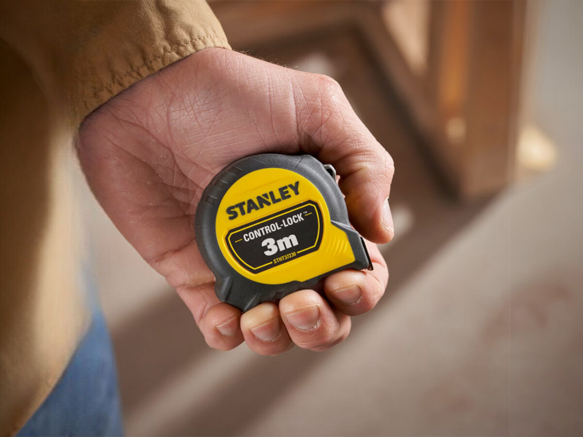 Osoba trzyma miarę zwijaną z widocznym logo \'STANLEY\' oraz napisem \'CONTROL-LOCK™ 3m STHT37230-0\'.