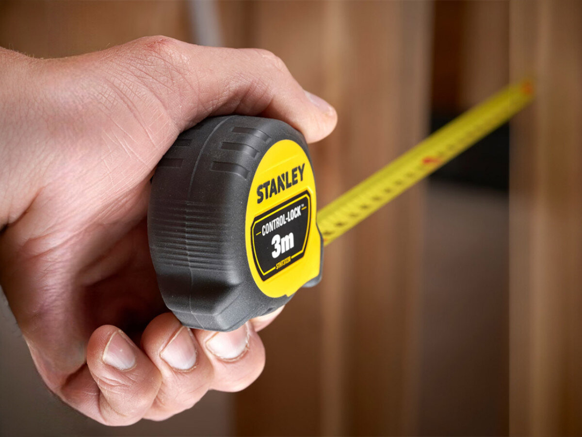 Osoba trzyma miarę zwijaną z widocznym logo \'STANLEY\' oraz napisem \'CONTROL-LOCK 3m\'.