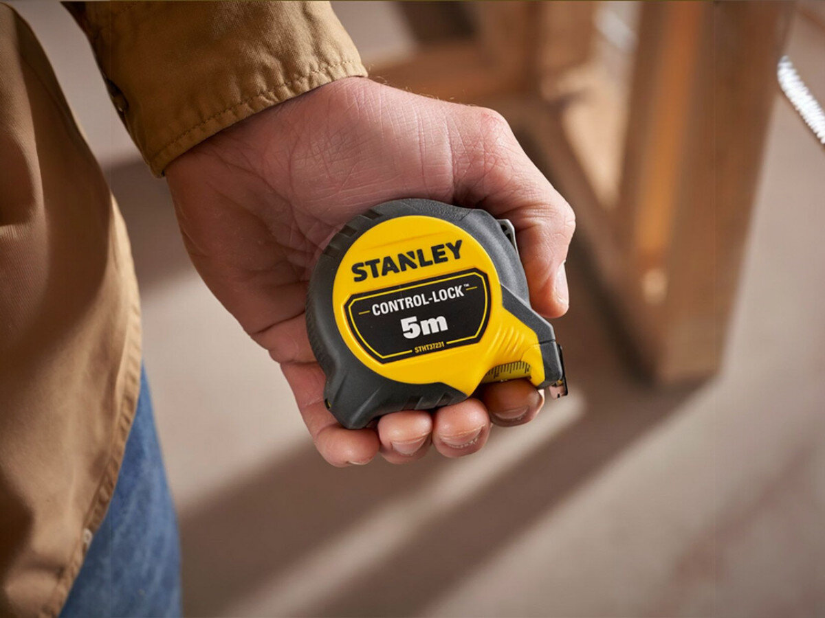 Osoba trzyma miarę zwijaną z napisem \'STANLEY CONTROL-LOCK 5m\'.