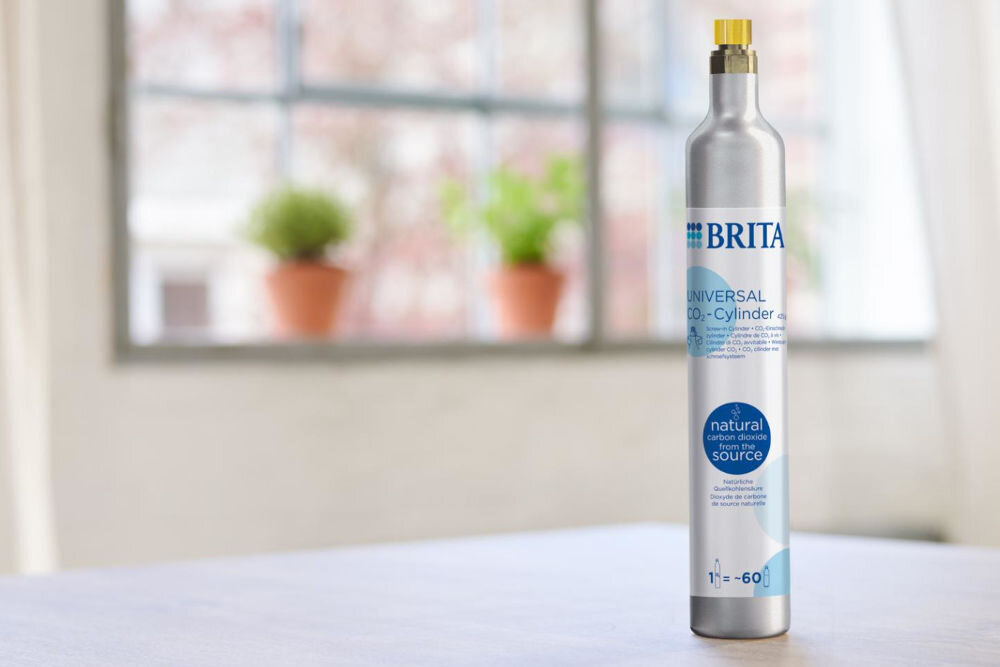 Nabój BRITA Sodaone CO2 1043744 na jasnym blacie stoi pionowo srebrny cylinder z gazem dwutlenkiem węgla, przeznaczony do urządzeń Brita do gazowania wody