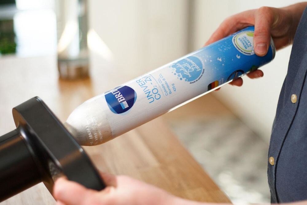 Nabój BRITA Sodaone CO2 1043744 ręce wkładające biały cylinder z gazem do saturatora Brita, z widocznymi napisami na naboju