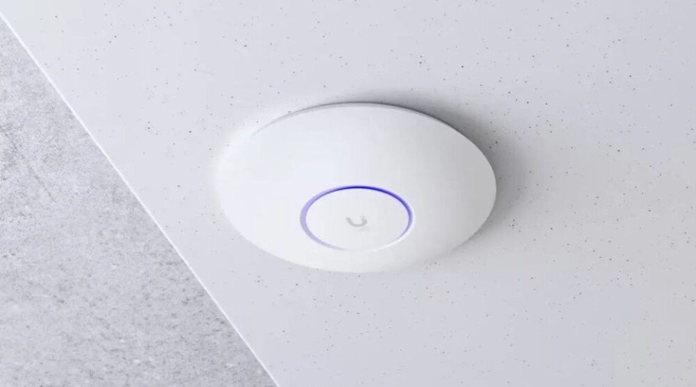 Punkt dostępu UBIQUITI U6 Enterprise Białe, okrągłe urządzenie sieciowe zamontowane na suficie z podświetlanym na niebiesko pierścieniem centralnym