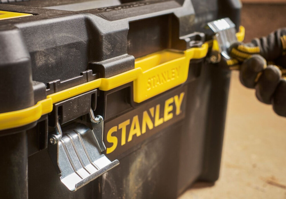 Skrzynia narzędziowa STANLEY STST83397-1 zbliżenie na zatrzaski osoba trzyma zatrzask w dłoni metalowe zatrzaski zabezpieczają zawartość przed przypadkowym otwarciem ochrona przed kurzem i innymi drobnymi zanieczyszczeniami