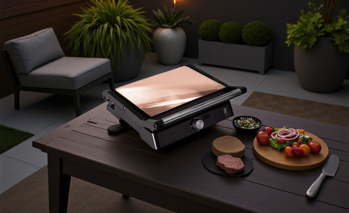 Grill elektryczny BERLINGER HAUS BH-9135, kuchnia, grillowanie, smażenie, gotowanie, Grill elektryczny BERLINGER HAUS BH-9135 z zamkniętą pokrywą w kolorze miedzianym, ustawiony na stole tarasowym, w otoczeniu donic z zielonymi roślinami.