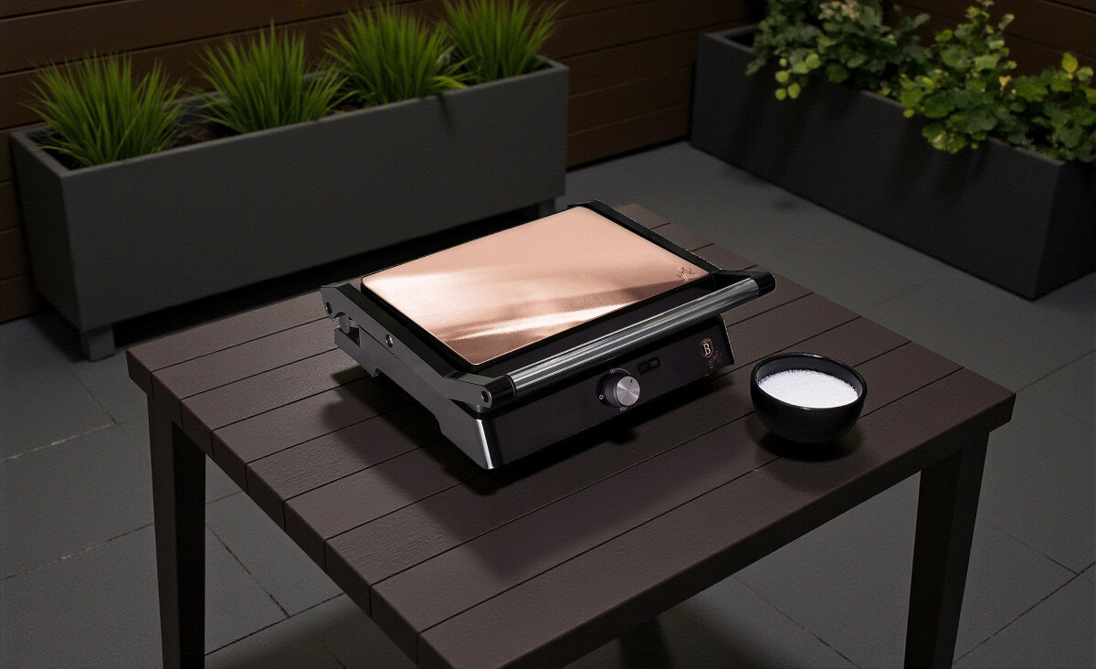 Grill elektryczny BERLINGER HAUS BH-9135, płasko, 180, ilość, większa, Grill BERLINGER HAUS BH-9135 z zamkniętą pokrywą stojący na tarasowym stole, obok miseczki oraz deski z warzywami i burgerami gotowymi do przyrządzenia.