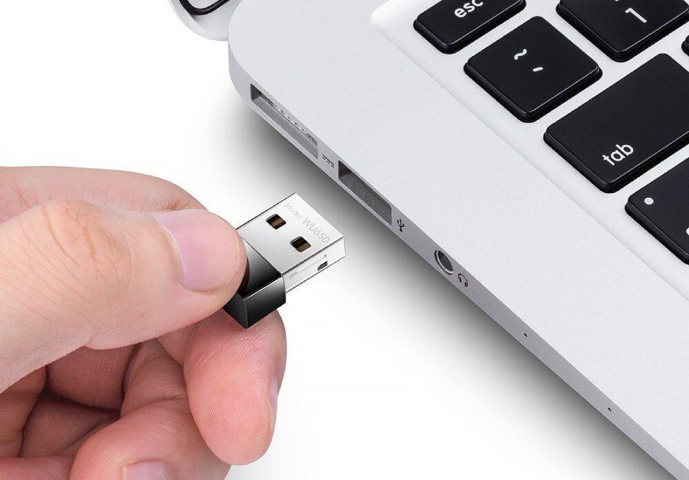 Karta sieciowa CUDY WU650 Ręka trzyma mały adapter USB z napisem modelu WU650 przed portem USB w obudowie srebrnego laptopa, opis