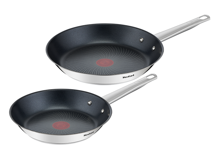 Na obrazie widoczne są dwie patelnie z czarnym wnętrzem i srebrnymi uchwytami. Na dnie patelni znajduje się czerwony okrąg z wzorem, a na boku widnieje logo \'Tefal\'.