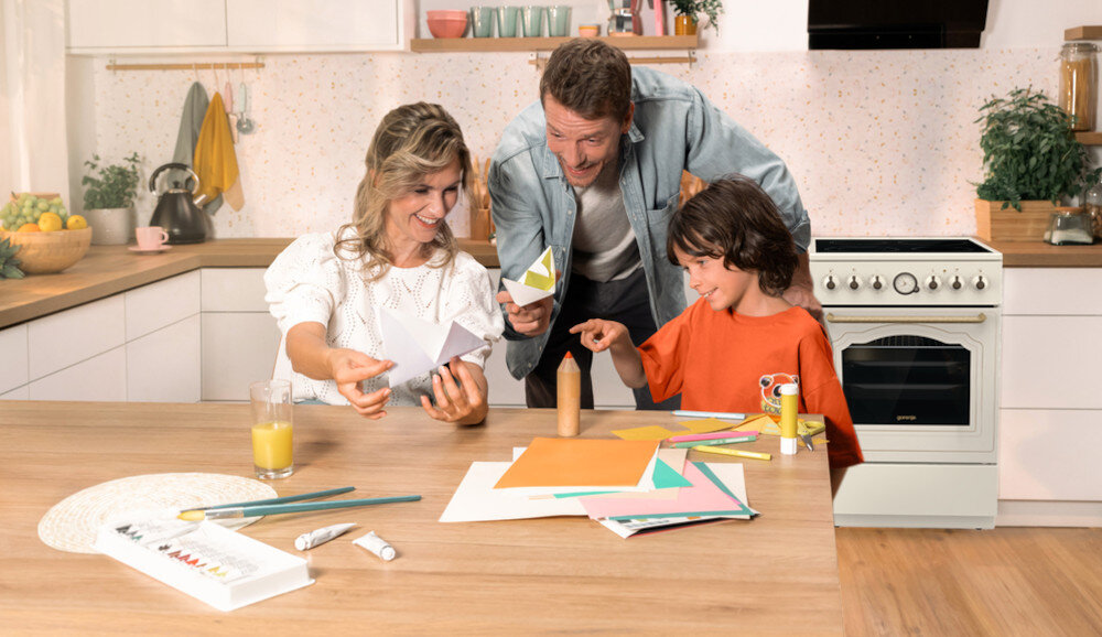 KUCHNIA GORENJE GECS6B70CLI lifestyle kuchnia rodzina dziecko akcesoria plastyczne na stole kuchenka w tle kolor czarno srebrny okap półki czajnik akcesoria kuchenne na blacie