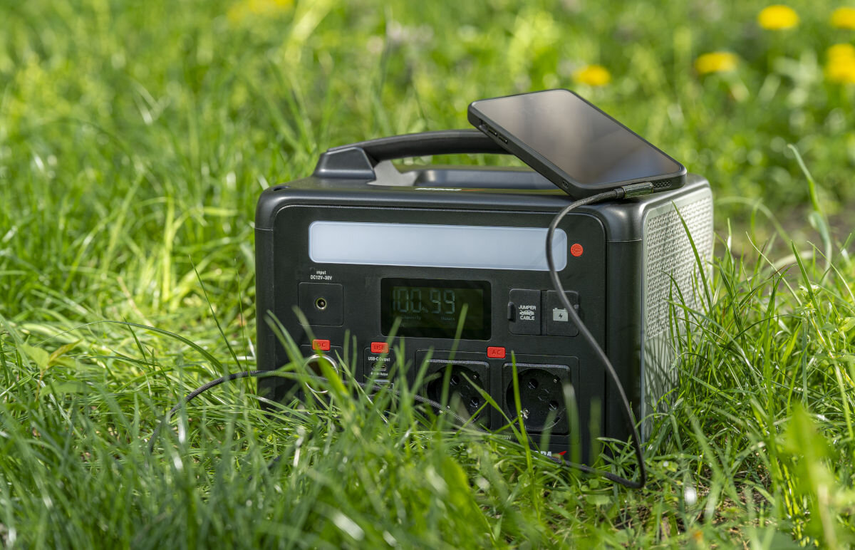 Stacja zasilania DEDRA DEZS0600 600W Bank energii panel fotowoltaiczny ładowanie, stacja w polu trawy z rozstawionym panele fotograficznym na sobie