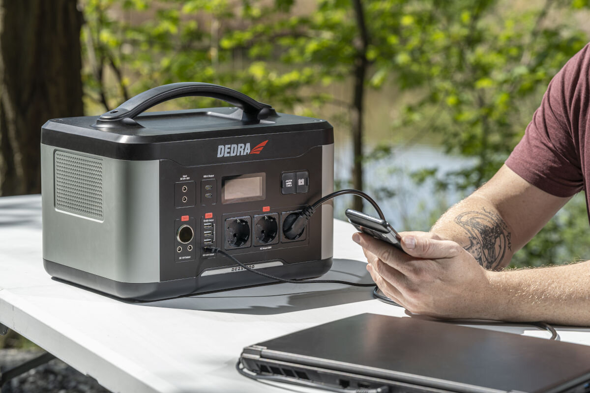 Stacja zasilania DEDRA DEZS1500 1500W Bank energii panel fotowoltaiczny ładowanie, stacja stoi na stole składanym z podpiętym smartfonem