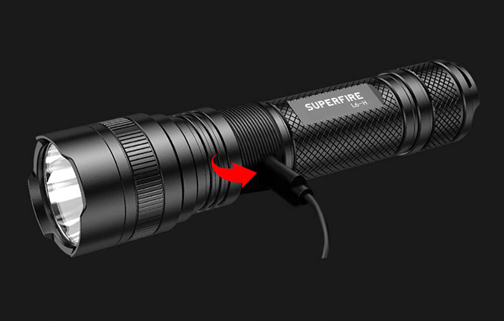 Czarna latarka z napisem \'SUPERFIRE L6-H\' jest podłączona do kabla USB-C. Obok portu ładowania znajduje się czerwona strzałka wskazująca na kabel.