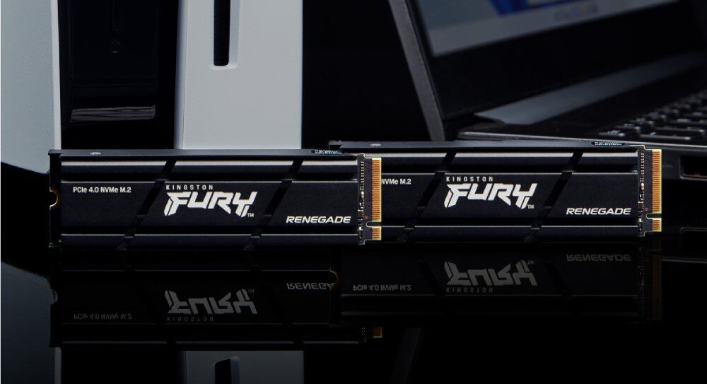 Dysk KINGSTON Fury Renegade Dwa podłużne dyski komputerowe leżące na czarnej, błyszczącej powierzchni obok laptopa i białej obudowy komputera, na podzespołach widać napis 'FURY', opis