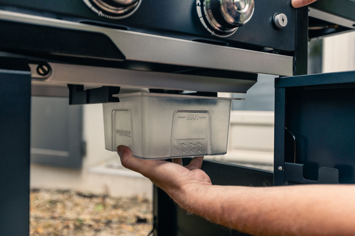 Grill gazowy CAMPINGAZ SELECT LX PLUS Seria 3, pojemnik, tłuszcz, odpady, resztki, dłoń trzyma pojemnik na tłuszcz i resztki
