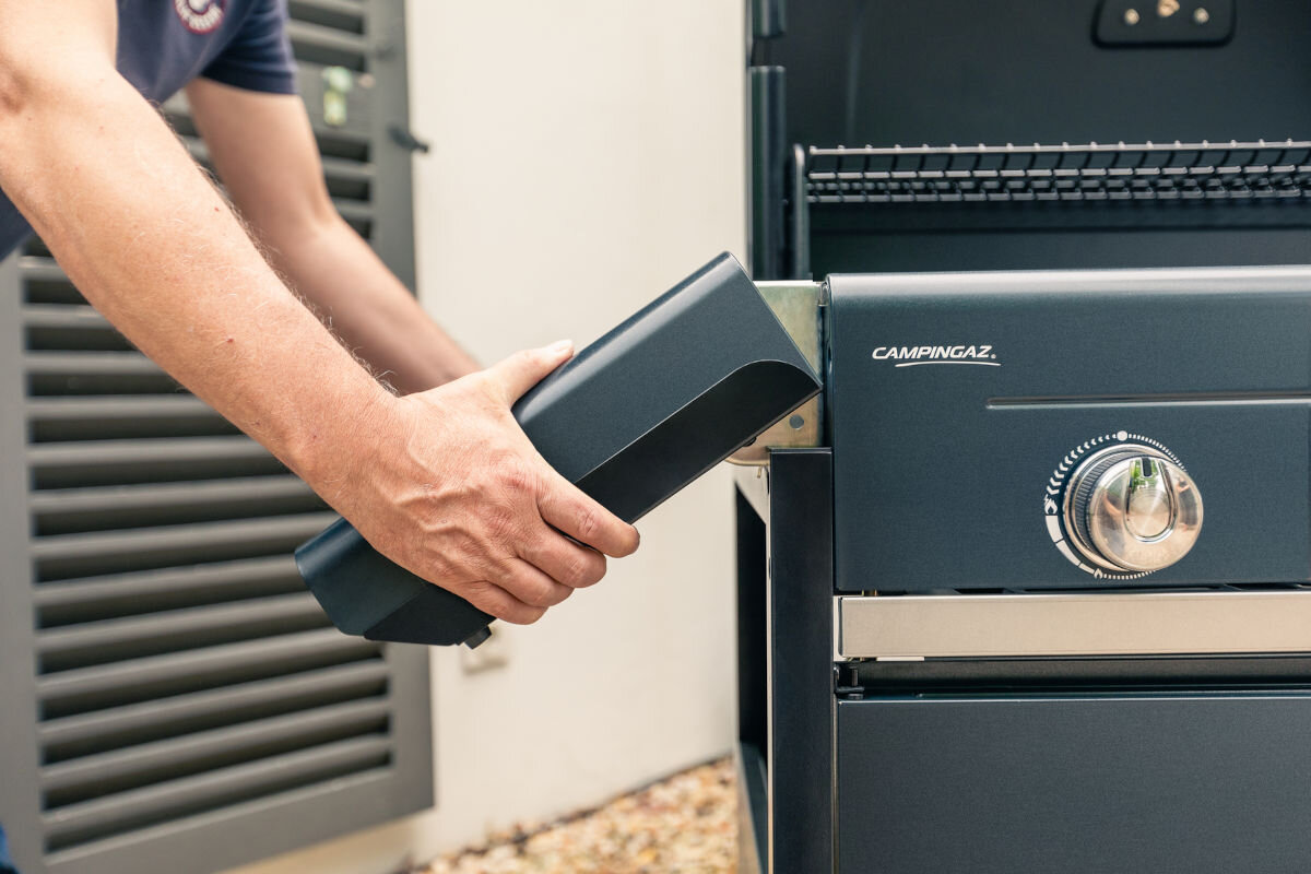 Grill gazowy CAMPINGAZ Select LX PLUS Seria 4 12 kW 46 x 72 cm, przestrzeń, przechowywanie, rozwiązanie, półki, wizualizacja składania półki bocznej grilla przez mężczyznę