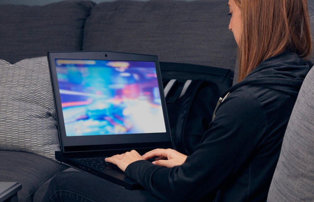 Pamięć RAM KINGSTON Fury Impact Kobieta siedząca na szarej kanapie trzyma na kolanach laptopa z włączoną grą na ekranie