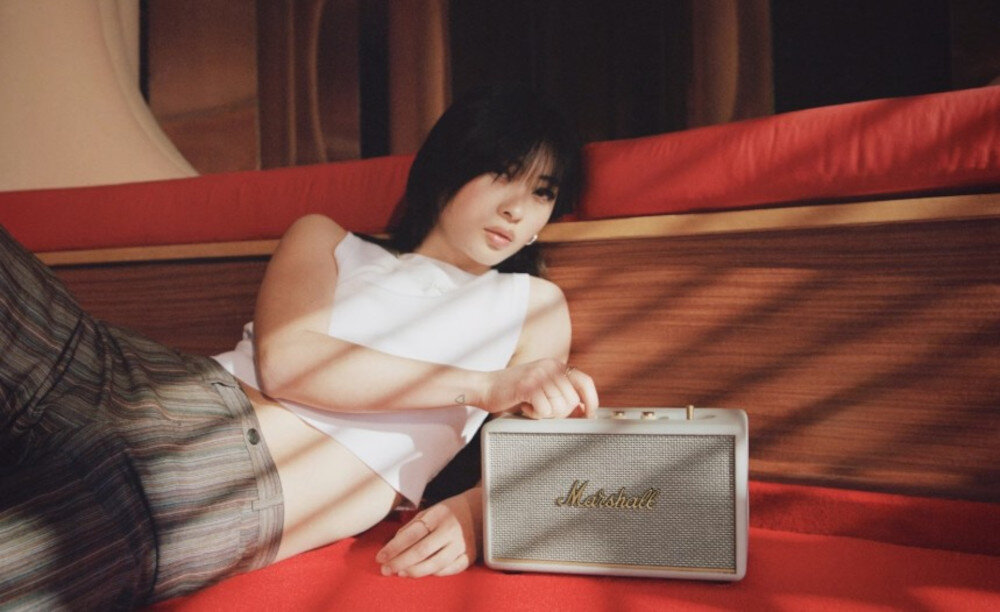 MARSHALL Acton III głośnik mobilny szerokie brzmienie stereo w pokoju, głosnik leżący na czerwonym dywanie, osoba leżąca obok głośnika