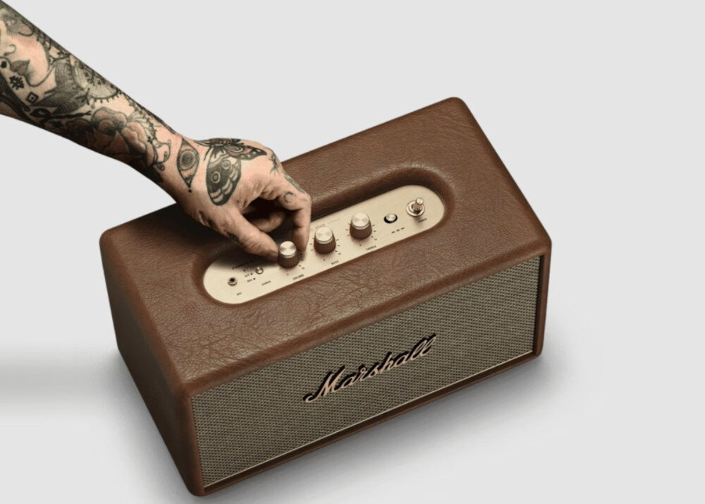 Głośnik MARSHALL STANMORE III sterowanie manualne pokrętła bas treble przyciski, głośnik stojący na szarym blacie, ręka trzymająca za pokrętło