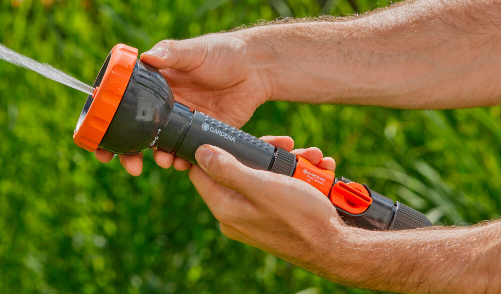 Zraszacz prosty GARDENA Profi-System trzyfunkcyjny z sitkiem 02847-20 rozmyte zielone tło osoba trzyma zraszacz w dłoniach zamyka dopływ wody zawór umożliwiający całkowite zamknięcie przepływu wody bez odłączania węża kontrola nad podlewaniem i myciem 