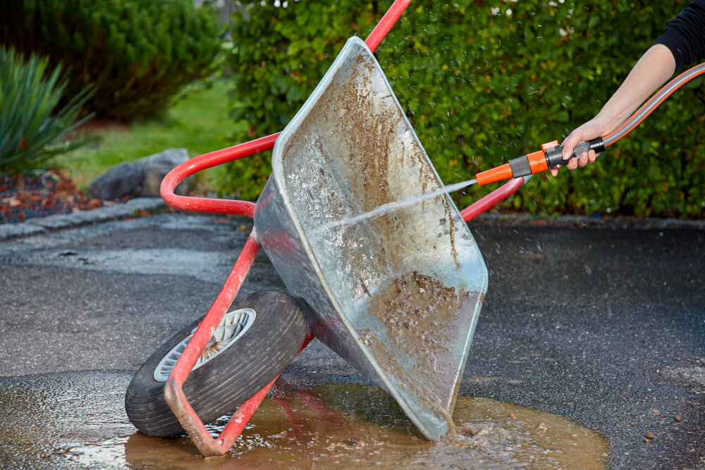 Pistolet zraszający GARDENA Profi-System 02818-20 ogród podjazd osoba myje taczkę za pomocą zraszacza w tle żywopłot krzewy trawnik rośliny podlewanie roślin czyszczenie powierzchni regulowany strumień wody od delikatnej mgiełki po punktowy strumień oszczędza czas i wysiłek